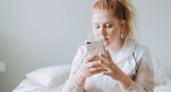 Eine junge Frau mit roten Haaren schaut interessiert auf ihr Smartphone